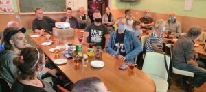 Na zdjęciu widać osoby siedzące wsp&oacute;lnie przy&nbsp;stole