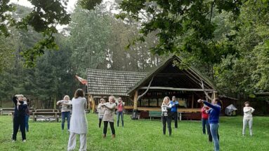 Grupa osób wspólnie ćwiczy na polanie