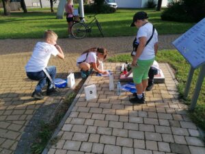 Grupa dzieci i&nbsp;młodzieży wsp&oacute;lnie rozwiązuje zagadki w&nbsp;plenerze