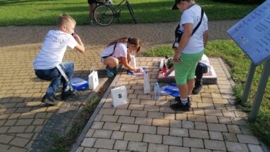 Grupa dzieci i młodzieży wspólnie rozwiązuje zagadki w plenerze