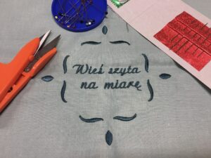 Zdjęcie przedstawia kawałek materiału z&nbsp;napisem "Wieś szyta na&nbsp;miarę"