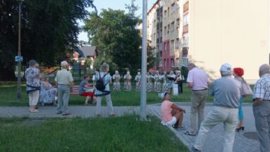 Zespół stojący w odległości od mieszkańców gra koncert