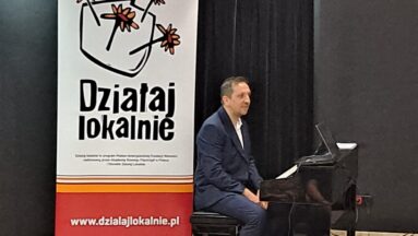Muzyk siedzący za pianinem w tle roll up Działaj Lokalnie