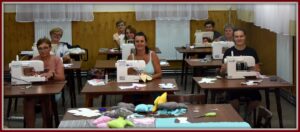 Na zdjęciu 8 stanowisk do&nbsp;szycia. Na&nbsp;kazdym stoliku jest maszyna do&nbsp;szycia na&nbsp;kt&oacute;rej pracuje osiem krawcowych